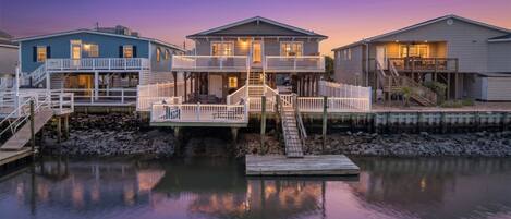 A waterfront property with multiple houses connected by walkways, featuring outdoor seating areas and a dock.
