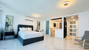 A modern bedroom with a large bed, a bedside table, and a chair. There is a bathroom with a mirror and a sink. - Apartment with Sea View in Isla Verde (Carolina)