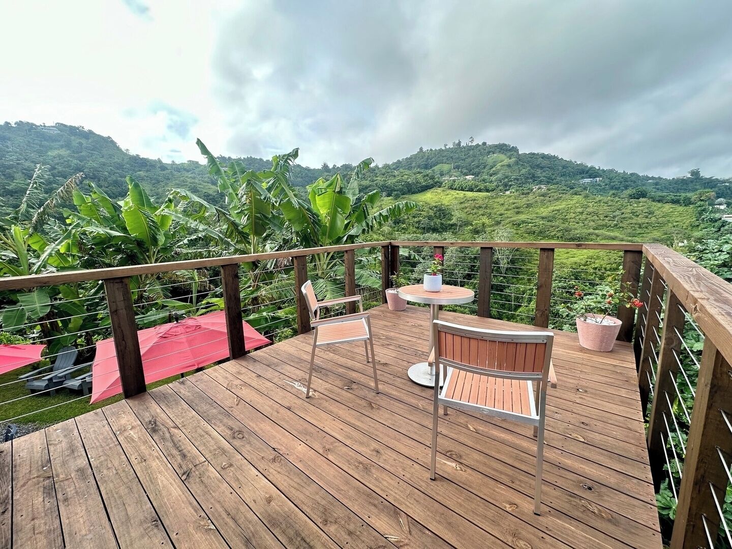 A wooden deck with outdoor seating, surrounded by lush greenery and hills in the background.
