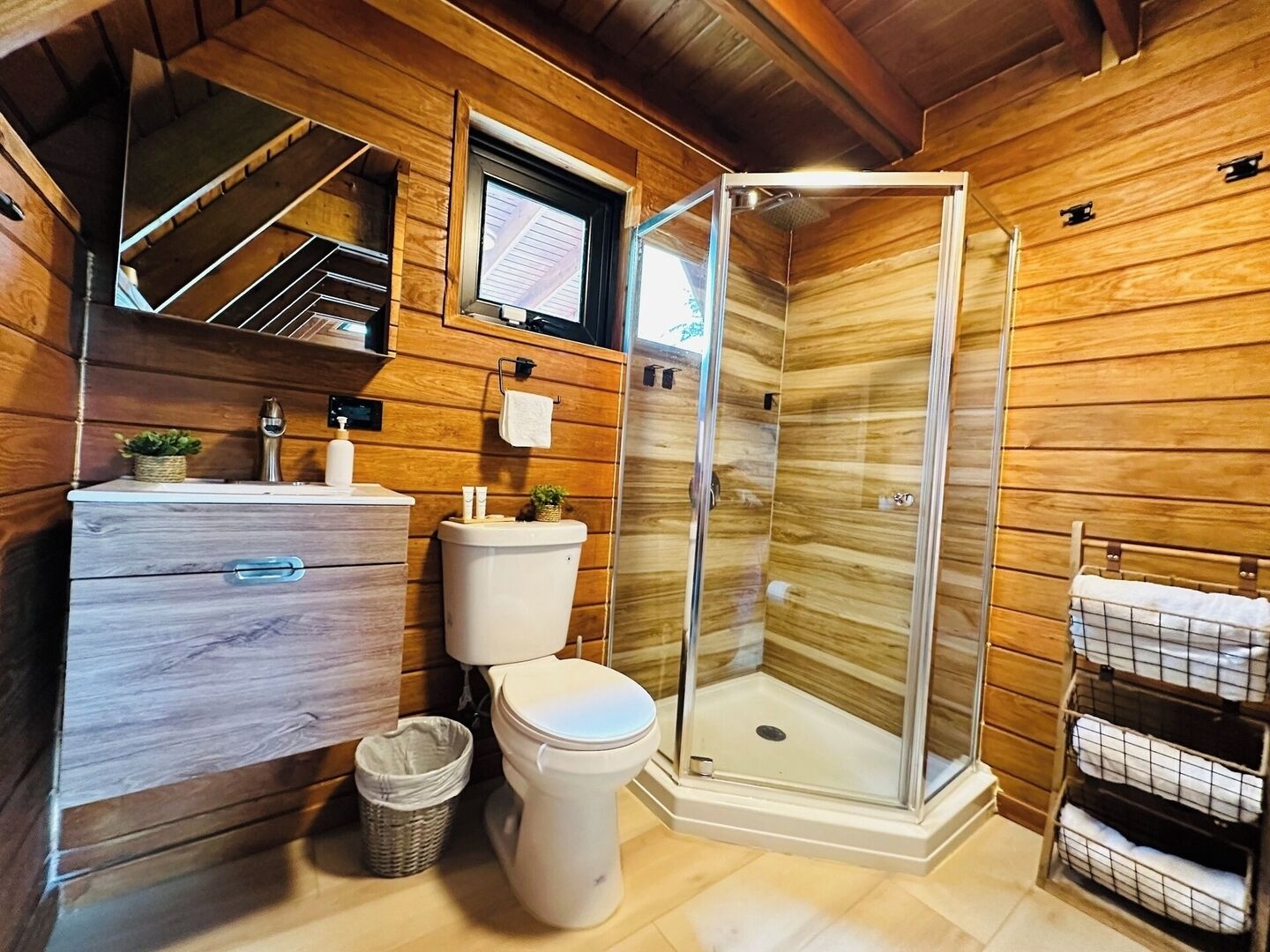 A wooden cabin bathroom with a wooden vanity, toilet, and a glass shower enclosure.