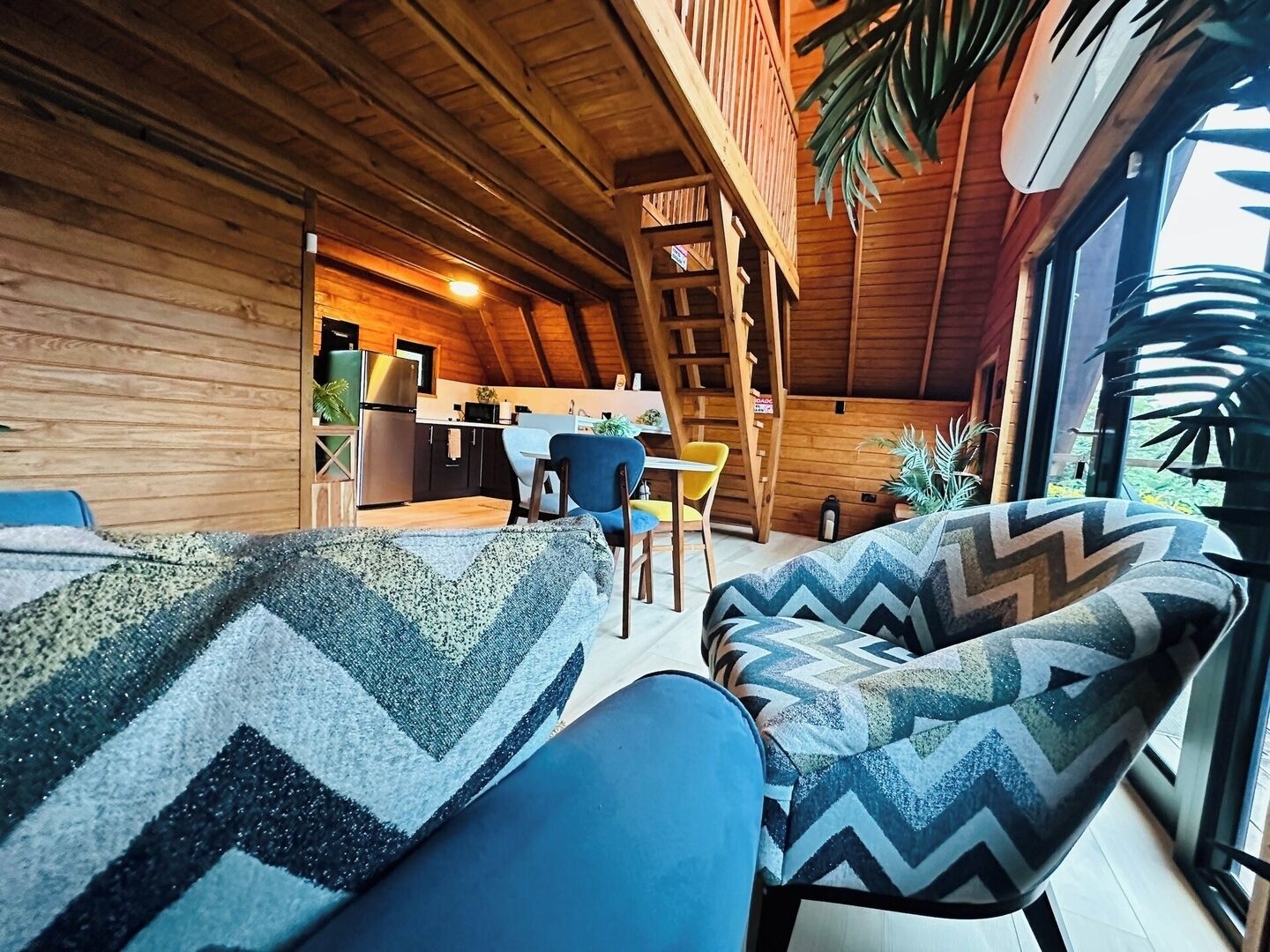 A cozy cabin interior with a dining area, kitchen, and a large window providing natural light.