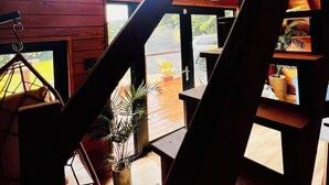 A wooden interior with a staircase leading to a balcony, a hanging chair, and a view of the outdoors. - Romantic Chalet Arcadia (Unknown)