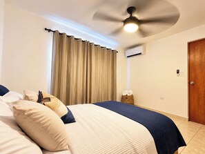 A bedroom with a bed, a ceiling fan, a window with curtains, and a door.