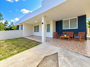 Une maison moderne dotée d’un patio couvert, d’une petite pelouse et d’un espace détente avec des chaises et une table.