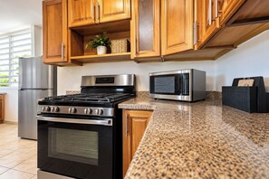 A kitchen with wooden cabinets, a stainless steel stove, a microwave, and a granite countertop.