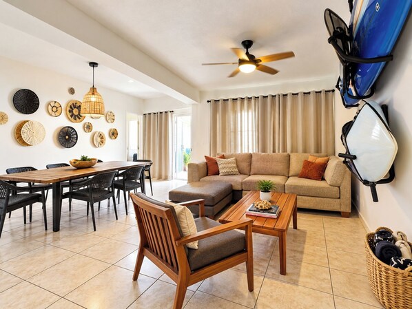 A living room with a sofa, coffee table, dining table, chairs, and a ceiling fan.