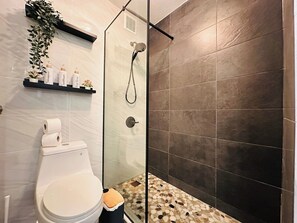 Un bagno moderno con doccia vetro, un water e uno scaffale con articoli da toilette.