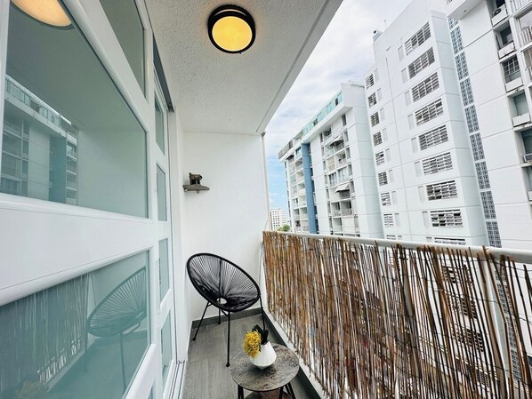 A balcony with a view of high-rise buildings, a round table with a vase, and a black chair.
