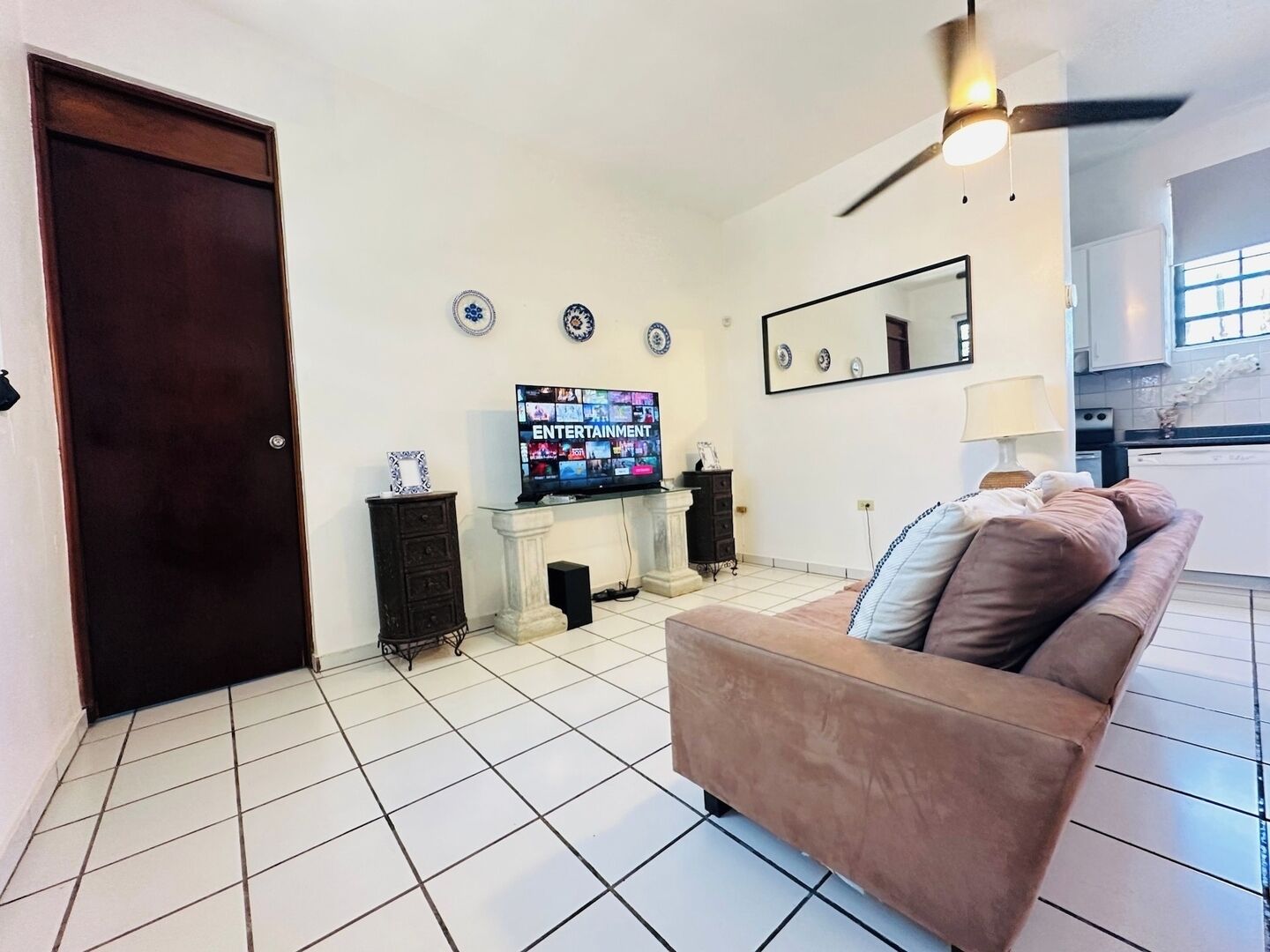 Ein Wohnzimmer mit Fernseher, einer Couch, einem Deckenventilator und einer Küche im Hintergrund.