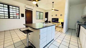 A kitchen with a central island, two ceiling fans, a TV, and a bar stool.