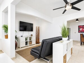 A modern living room with a black leather sofa, a flat-screen TV, a ceiling fan, and a white entertainment unit.
