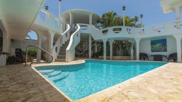 A swimming pool with a stone deck, a staircase, and a covered seating area with a mural.