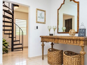 A staircase with a black railing, a wooden console table with decorative items, a mirror, and wicker baskets. - CasaPlaya Gamil Rene (Barceloneta)