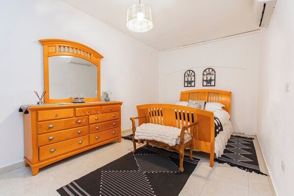 Een slaapkamer met een houten dressoir, een stoel, een bed en een zwart-wit kleed.