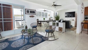 A spacious living area with a dining table, chairs, and a kitchen area with a TV.