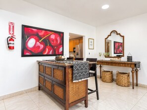 A dining area with a large painting of red apples, a fire extinguisher, a wooden console table, and a mirror. - CasaPlaya Gamil Rene (Barceloneta)