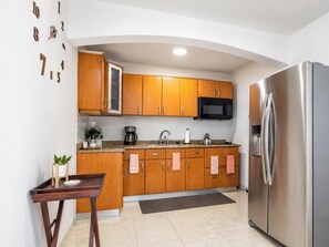 A modern kitchen with wooden cabinets, stainless steel appliances, and a small dining table. - CasaPlaya Gamil Rene (Barceloneta)