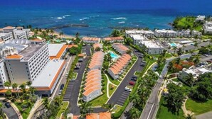 An aerial view of a resort with multiple buildings, a parking area, and a view of the ocean.