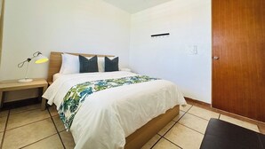 A bedroom with a bed, bedside table, lamp, and a wooden door. - Paradise Beach Apartment Vieques 6 (Vieques)