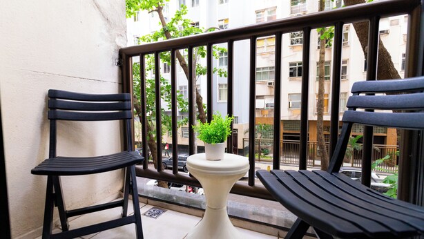A balcony with two black chairs, a white pedestal table with a potted plant, and a view of a residential building.