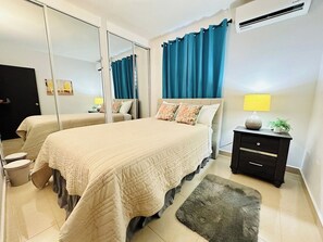 A modern bedroom with a large bed, a bedside table with a lamp, a small plant, and a mirror.