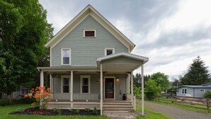 A two-story house with a porch, a small front yard with a flower bed, and a driveway.