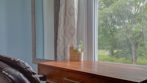 A wooden desk with a drawer, a potted plant, and a window with a view of trees.