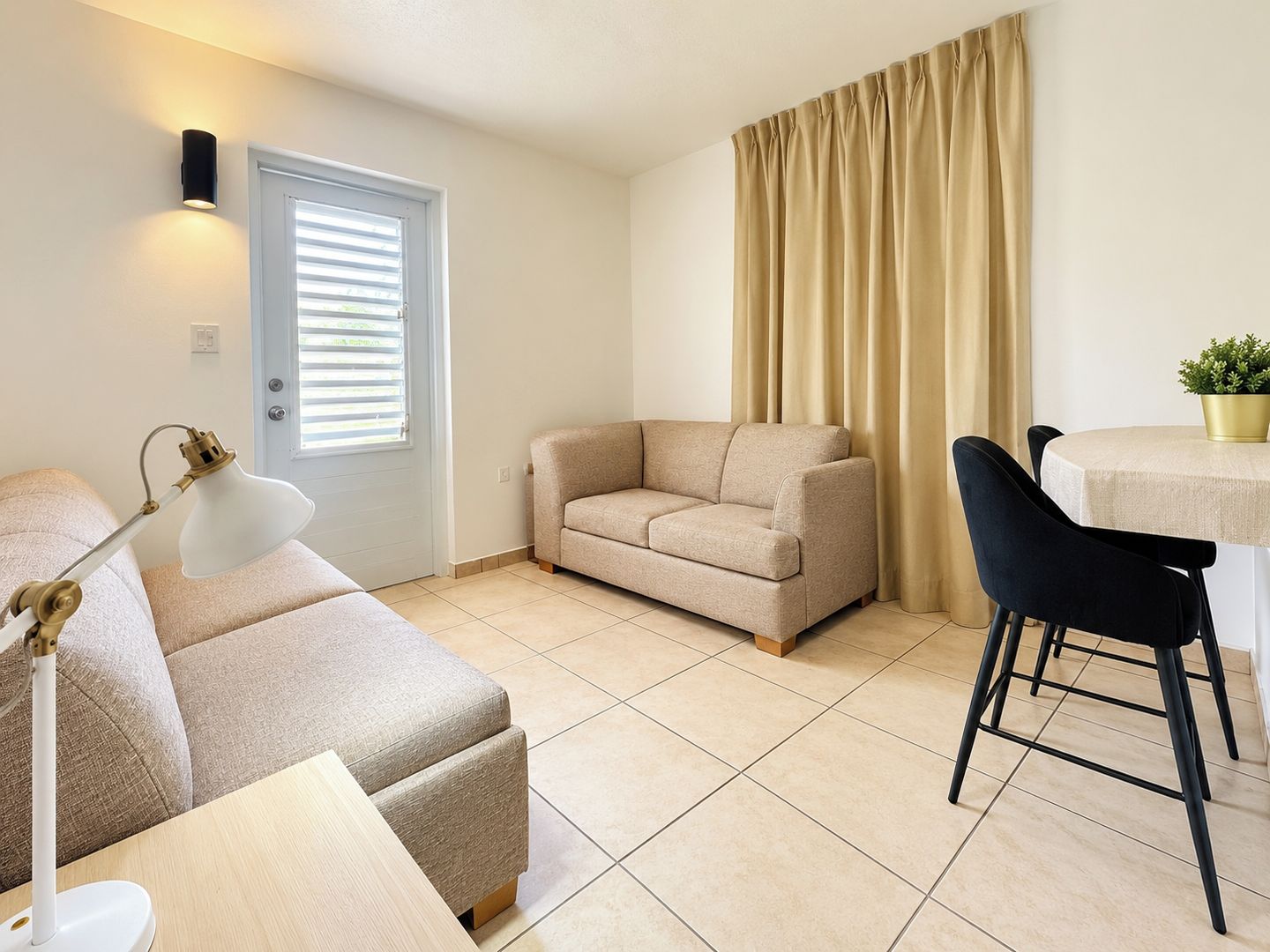 A living room with a beige sofa, a black chair, a small table with a plant, and a lamp.