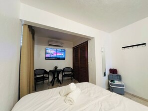 Une chambre d’hôtel avec un lit, un téléviseur fixé au mur, une petite table avec deux chaises et une poubelle.
