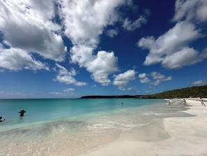 Una platja amb aigua turquesa cristal·lina, sorra blanca i un turó a la distància.