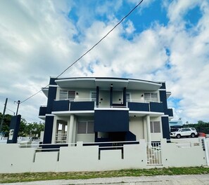 Une maison moderne à deux étages, dotée d’un toit plat, d’un balcon et d’une entrée sécurisée par un portail.