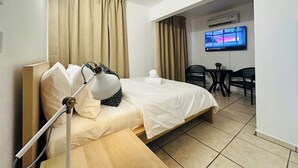 Habitación de hotel con cama, escritorio, silla, televisor y cortinas.