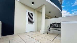 Un espacio exterior limpio y moderno con una puerta blanca, un banco y un suelo de baldosas.