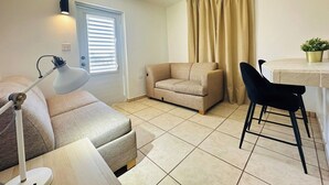 Una sala de estar con sofá, sillón, lámpara, ventana con persianas y cortina.