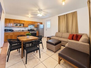 Un espacio habitable compacto con kitchenette, una zona de comedor con mesa y sillas, un sofá y una ventana con cortinas.