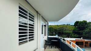 A balcony with a table and chairs, a white air conditioner, and a view of a green landscape. - Paradise Beach Apartment Vieques 5 (Vieques)