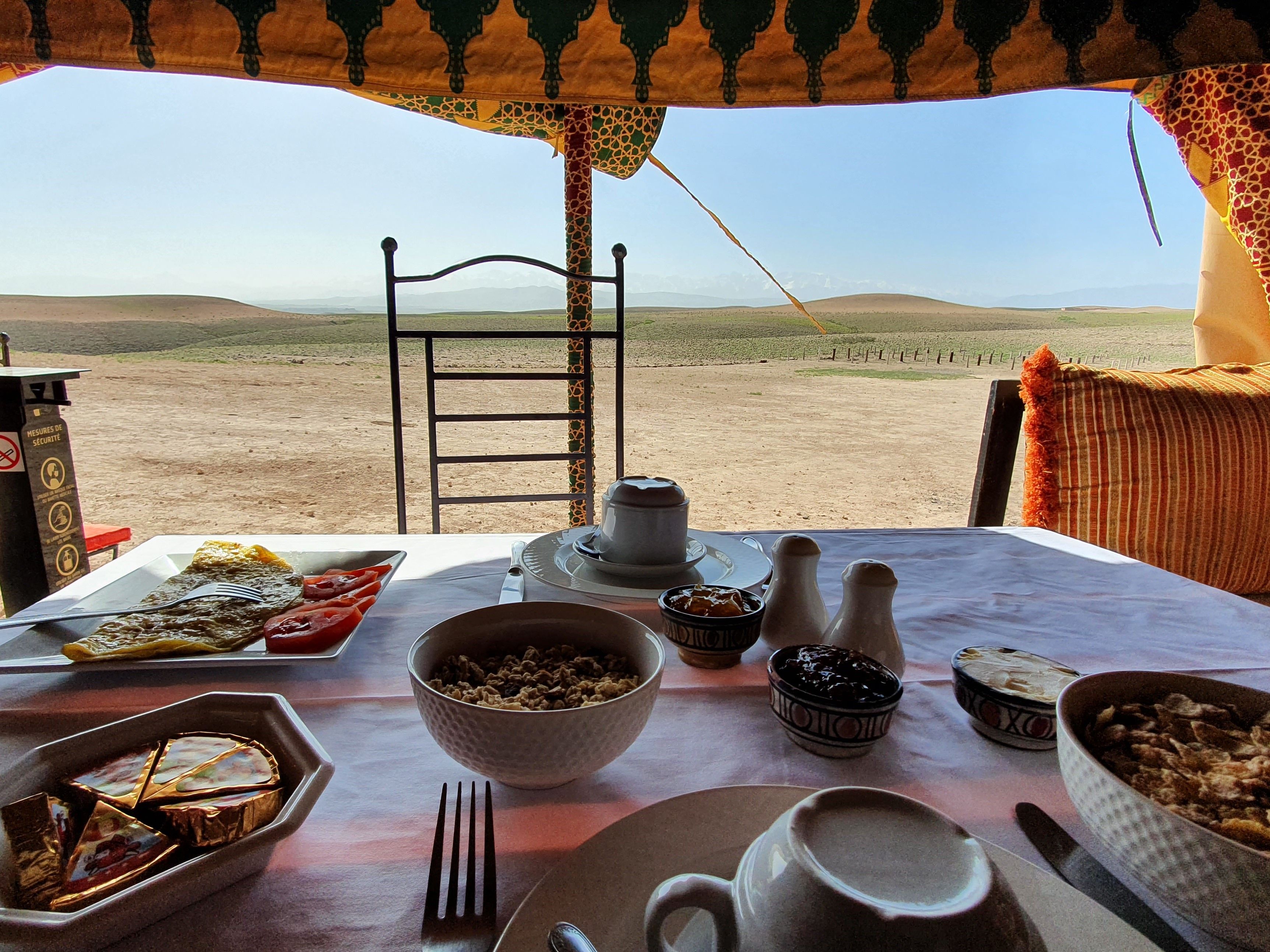 A dining table set with various dishes and utensils, a chair, and a view of a desert landscape.
