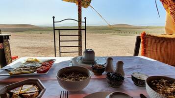 A dining table set with various dishes and utensils, a chair, and a view of a desert landscape.