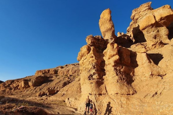 A rocky landscape with a person standing near a large rock formation. - Nkhila Lodge (Sidi Badhaj)