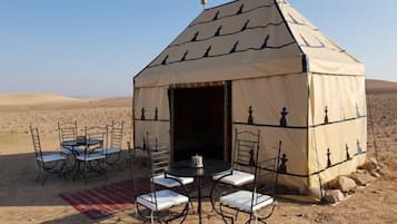 A tent with a chessboard design, equipped with tables and chairs, set in a desert.