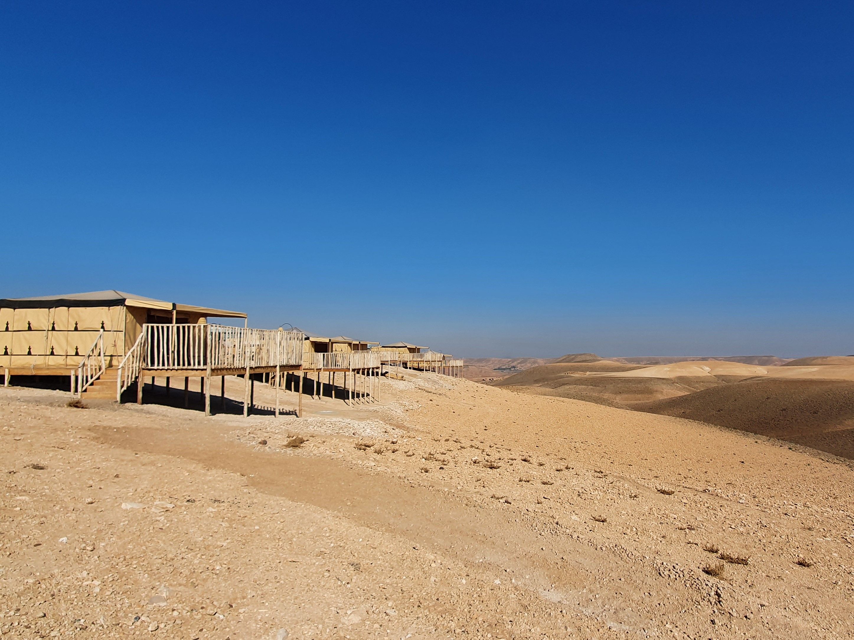 A desert landscape with a row of beige tents connected by wooden walkways.