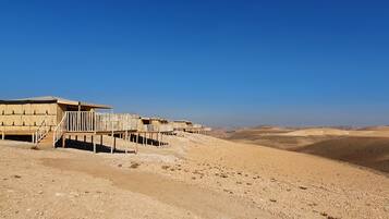 A desert landscape with a row of beige tents connected by wooden walkways.