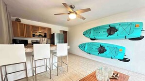 A modern kitchen with wooden cabinets, a dining area with white chairs, and two kayaks mounted on the wall.