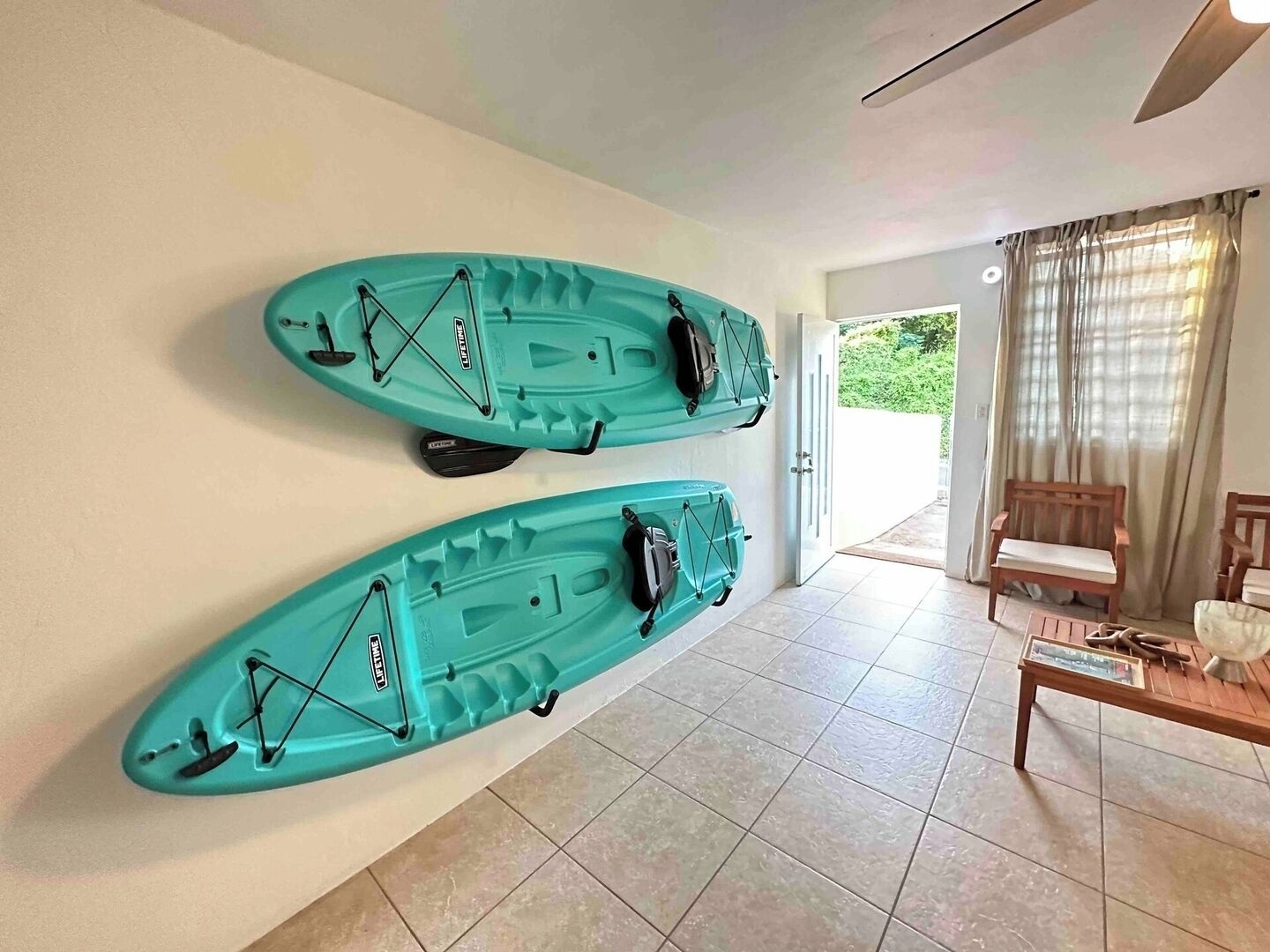 Habitación con dos kayaks colgados en la pared, un banco de madera y vista a zonas verdes al exterior.