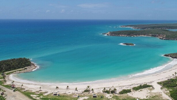 A coastal landscape with a sandy beach, clear turquoise waters, and a small island.