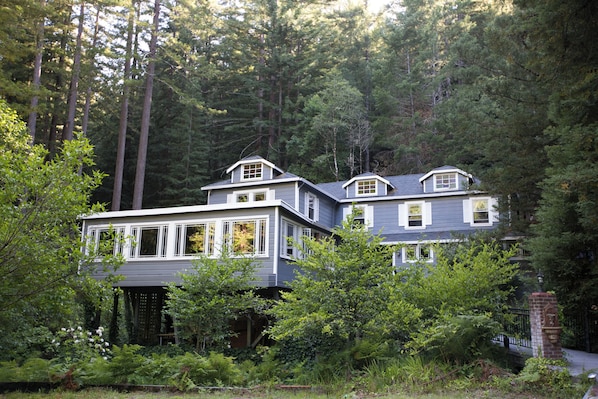 A two-story house with a covered porch, surrounded by dense forest.