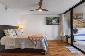 A bedroom with a bed, a ceiling fan, a wall-mounted TV, and a window with a view of a waterfall. - Ocean View Walk to Mall Free Parking, W/D, AC (Aiea)