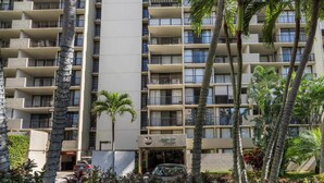 A multi-story hotel with balconies, palm trees, and a parking area.
