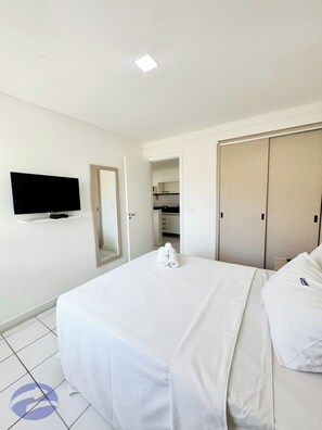 A hotel room with a bed, a television mounted on the wall, a wardrobe, and a bathroom visible through an open door.