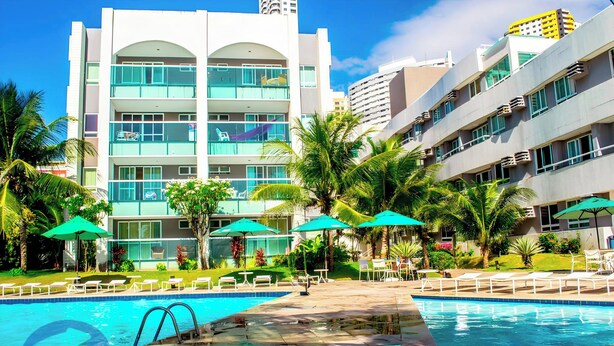 A hotel with a pool area, outdoor seating, and palm trees. -  Ponta Negra Beira Mar - Pimentel (Natal)